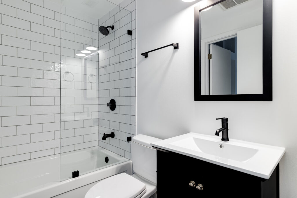 A small modern bathroom with a dark vanity, mirror frame, and handle by LHS Remodeling & Design